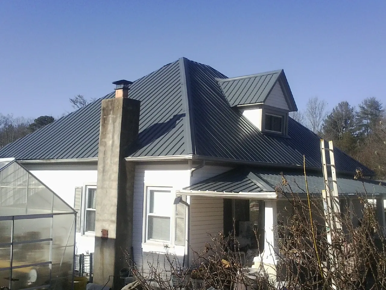 Dark blue standing seam metal roof on a white farmhouse with dormer — Slate & Tile Roof Repair by Roofing Brothers in Wrightwood