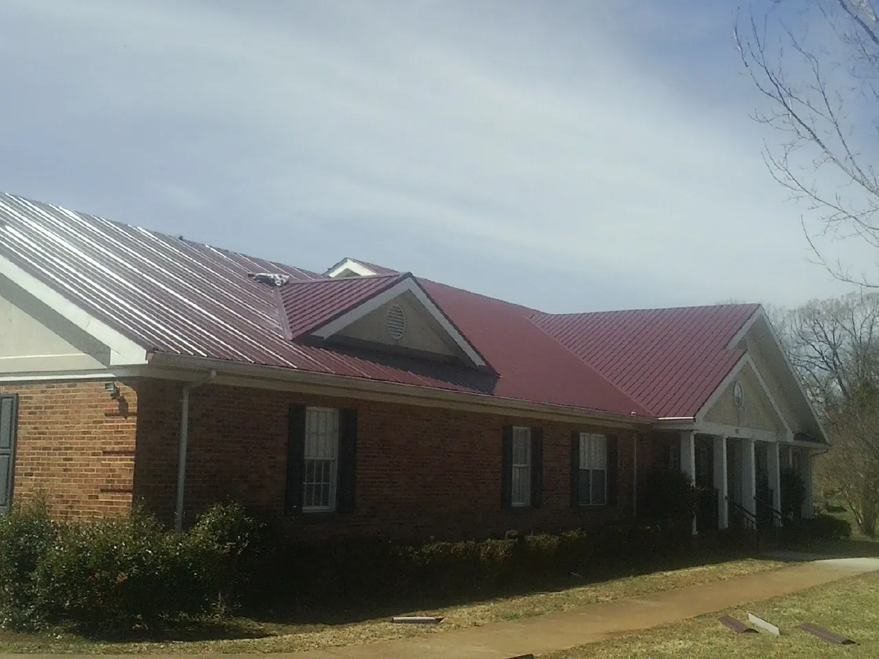Red metal roof with gabled entries on a long brick building, from a Hail Damage Roof Repair job in Wrightwood