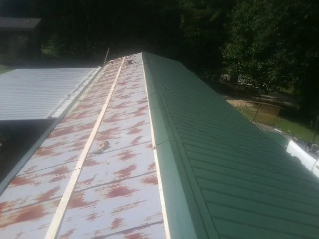 Old rusted panels beside newly installed green metal roofing — Wind Damage Roof Repair by Roofing Brothers in Wrightwood