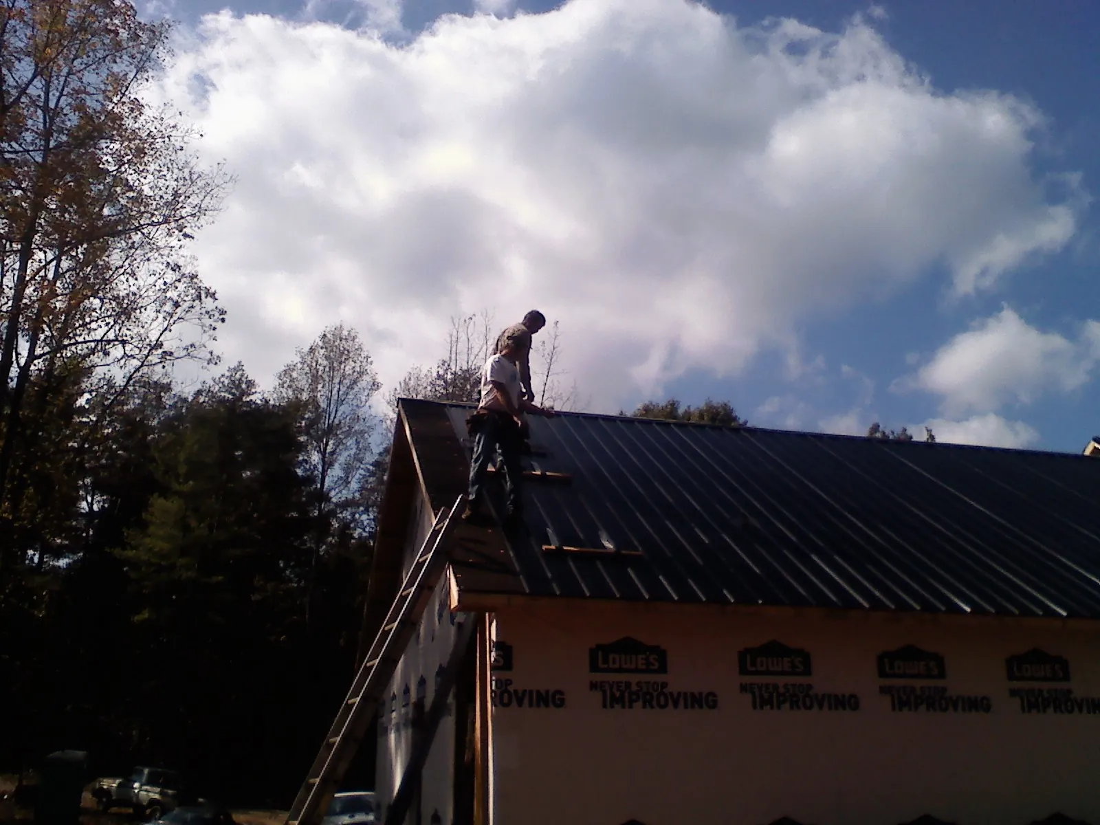 Roofer fastening dark metal panels high against a cloudy sky, from a Roof Inspection job in Wrightwood