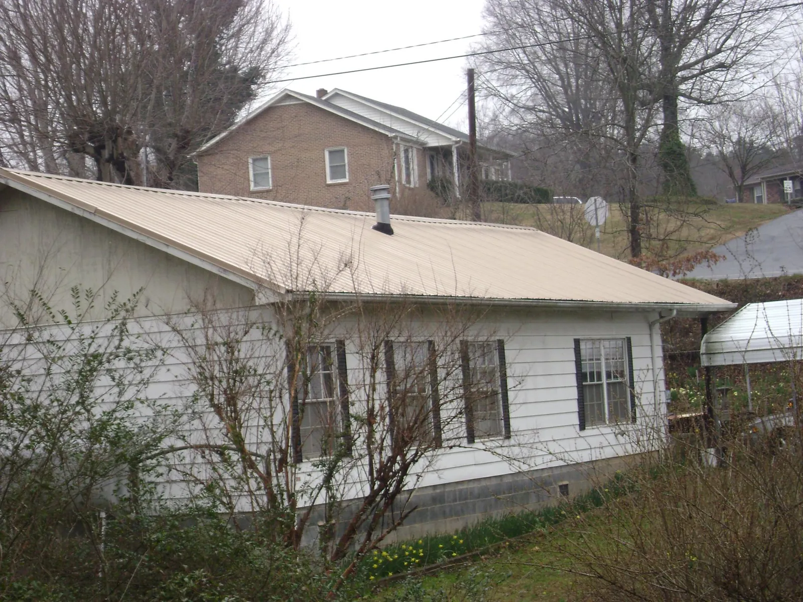 Tan metal roof on a white sided house set into a hillside — Commercial Roofing by Roofing Brothers in Wrightwood
